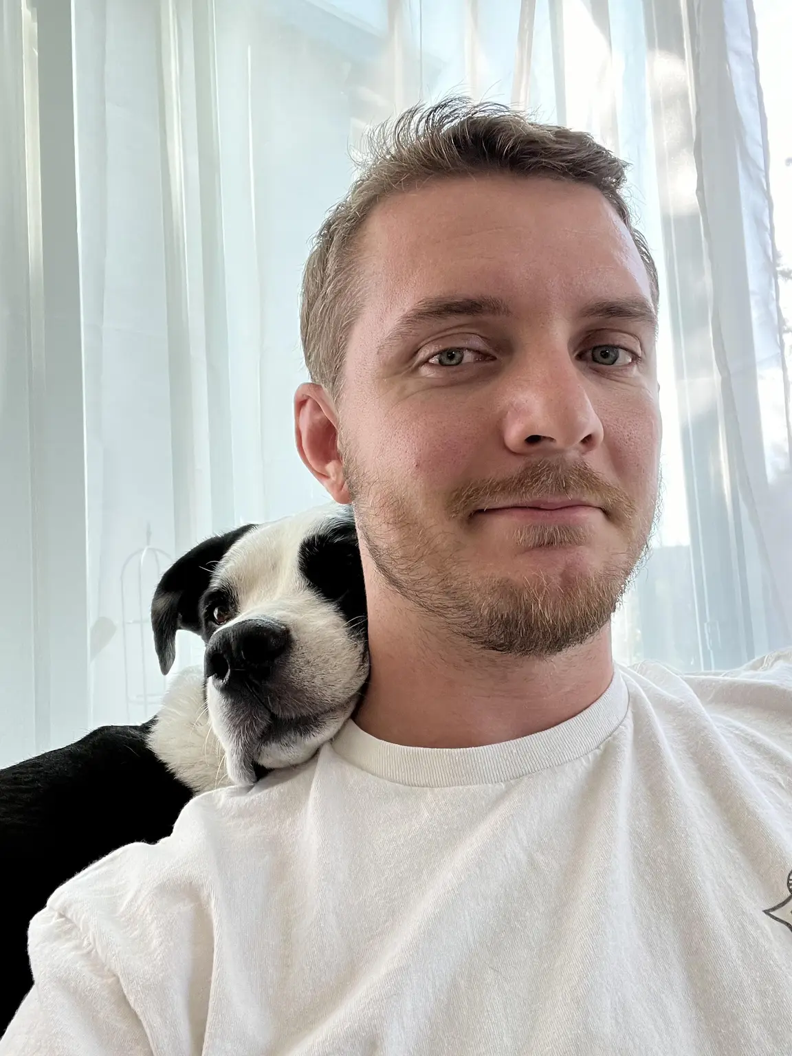 Chase at home with a black-and-white dog resting on his shoulder